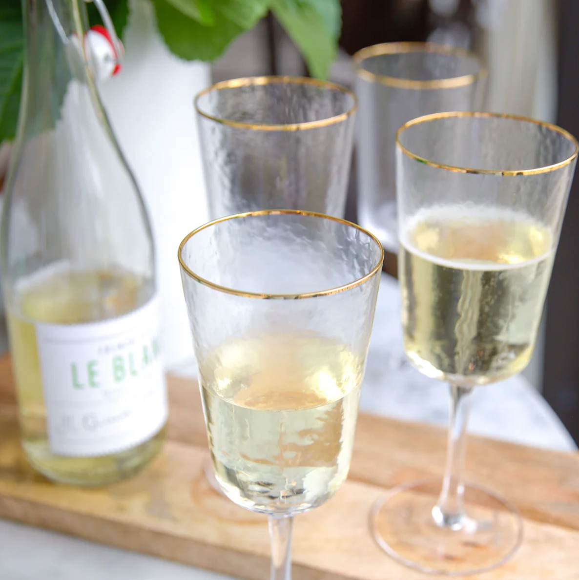Champagne glasses with gold rims on a wooden board, filled with champagne, next to a bottle labeled 'Le Bel'.